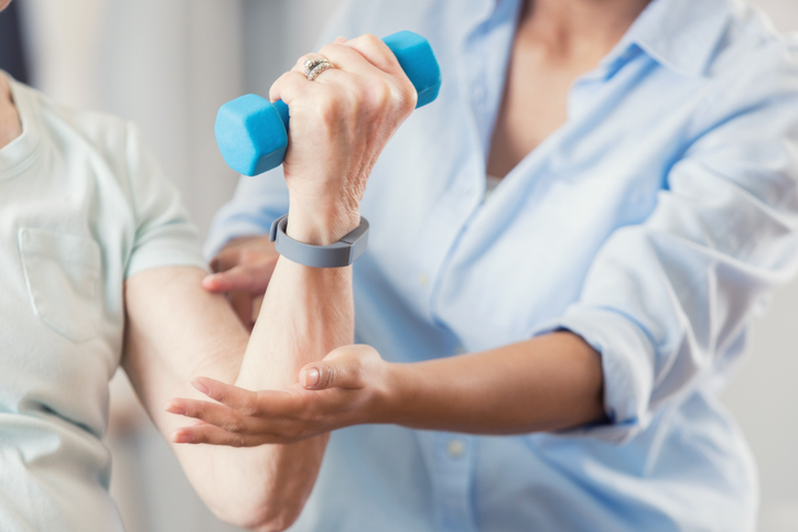 Physical therapist works with senior woman. The patient is using a hand weight.