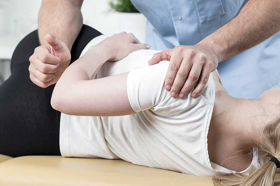 Oakville Chiropractor, female patient on her side with the chiropractors working on her hip and shoulder