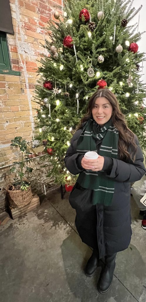 Photo of psychotherapist Alessia Zita. Nice smile, holding a hot chocolate, dressed cozy in front of a Christmas tree