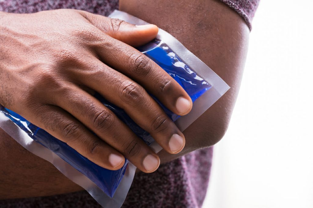 Close-up Of A Person Applying Ice Gel Pack On An Injured Elbow Against White Backdrop
