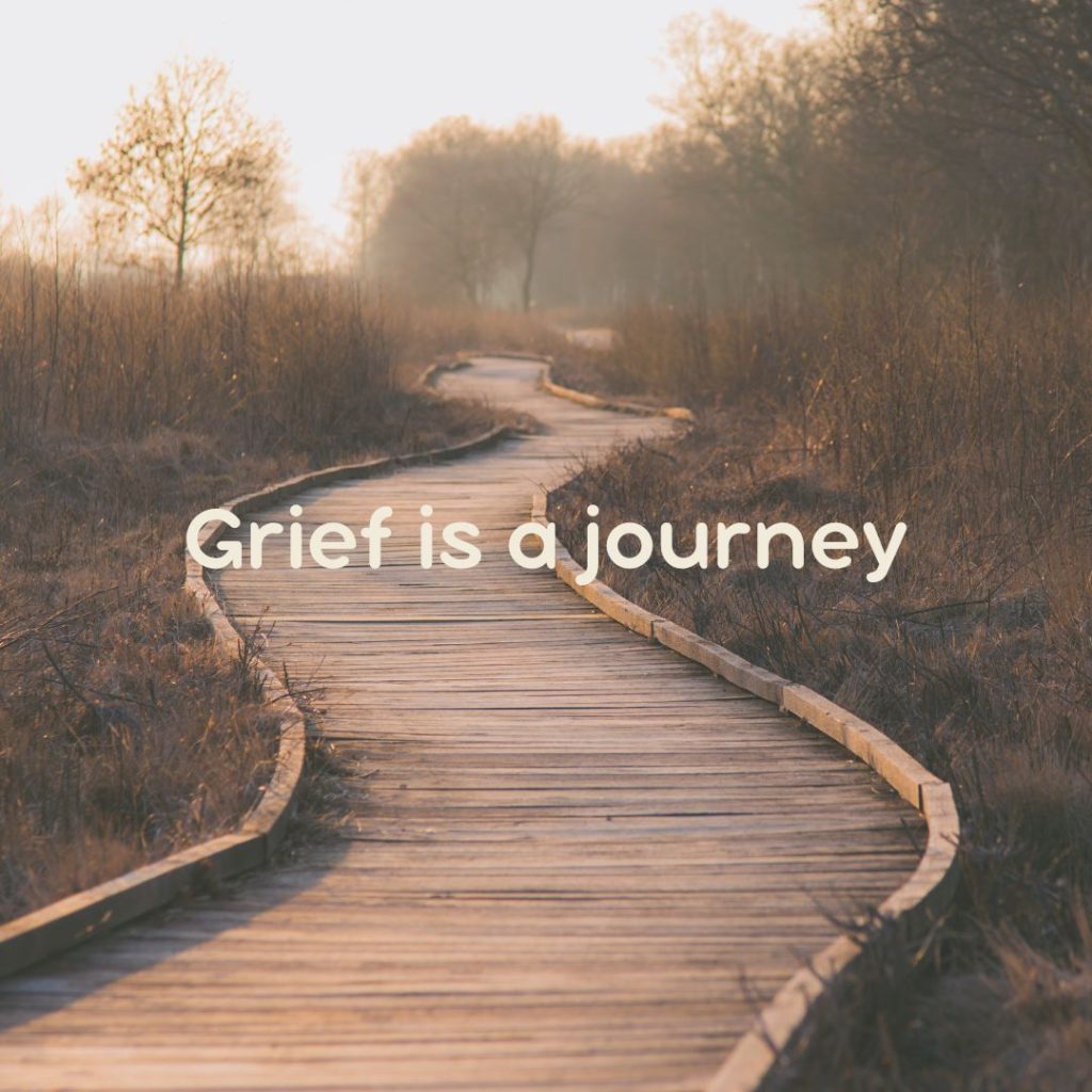 A photo of a trail in a forest that is foggy and says grief is a journey