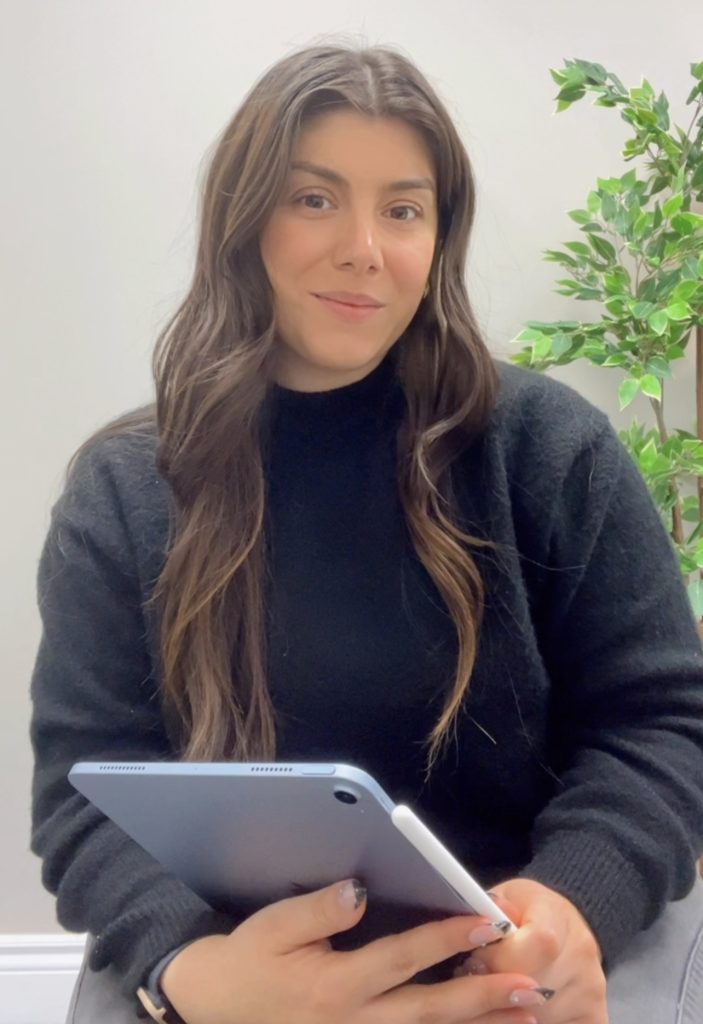 Picture of psychotherapist Alessia Zita. Nice smile, long brown wavy hair, holding an iPad.